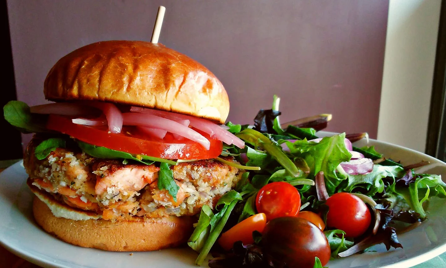 A Flat Iron Tap burger with tomato and red onion, served with a fresh side salad